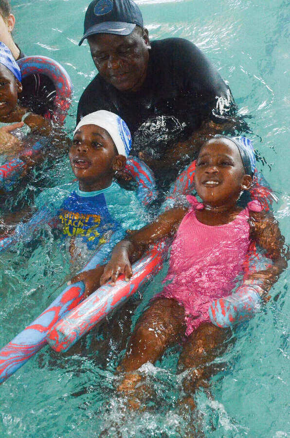 Kiddies Aqua instructor working with two young swimmers supported by a pool noodle
