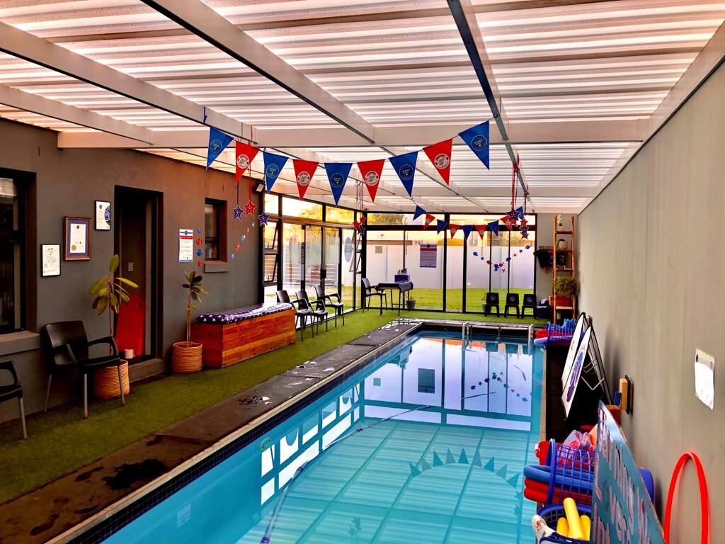 Indoor heated pool decorated with festive branded bunting, with poolside seating, artificial turf and learn-to-swim equipment ready for lessons.
