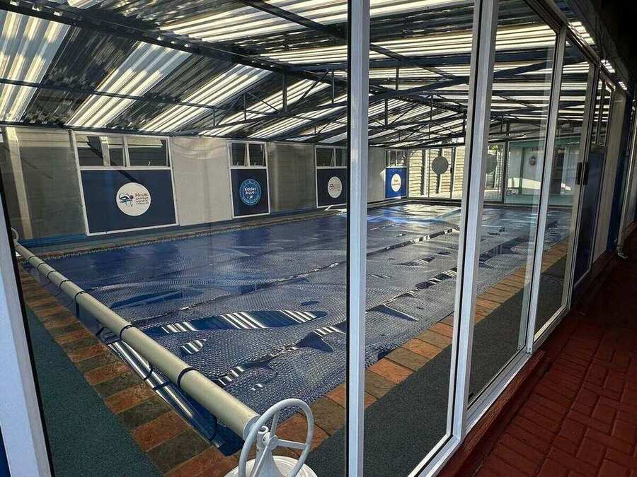 Enclosed pool protected by a rolling thermal blanket, viewed through glass sliding doors that keep the heated water warm year-round.