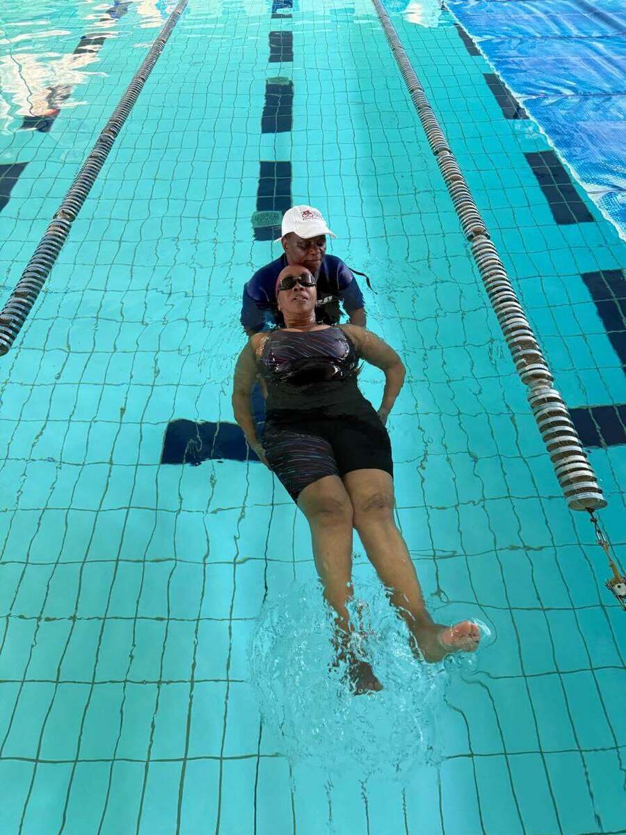 Adult learner floating on their back with a Kiddies Aqua instructor's support in the lap pool