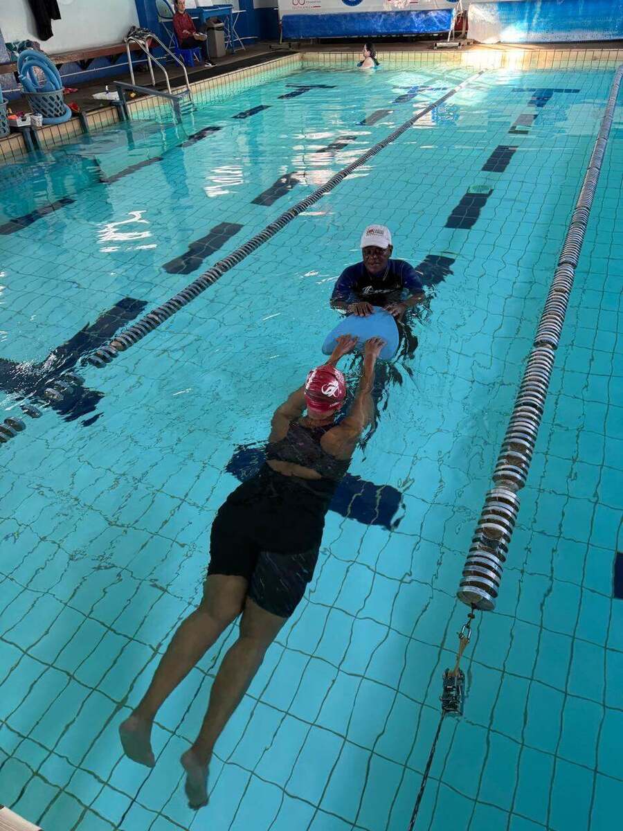 Adult swimmer practising a kickboard drill across the lap pool with a Kiddies Aqua instructor