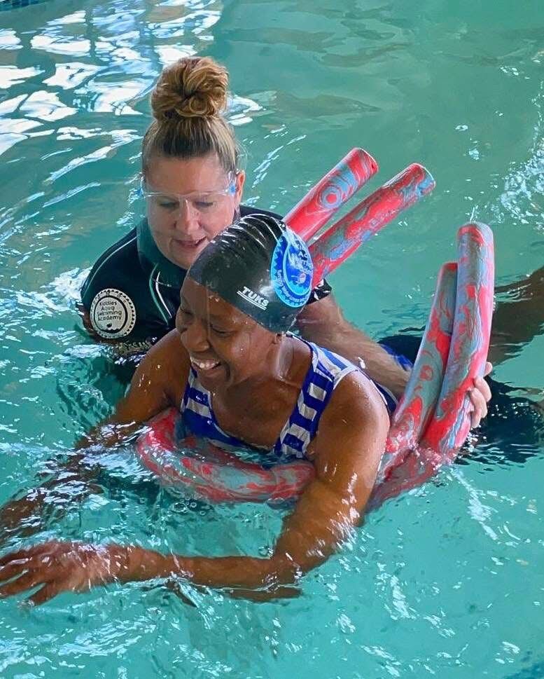 Adult learner supported on pool noodles by a Kiddies Aqua instructor during a private adult swimming lesson